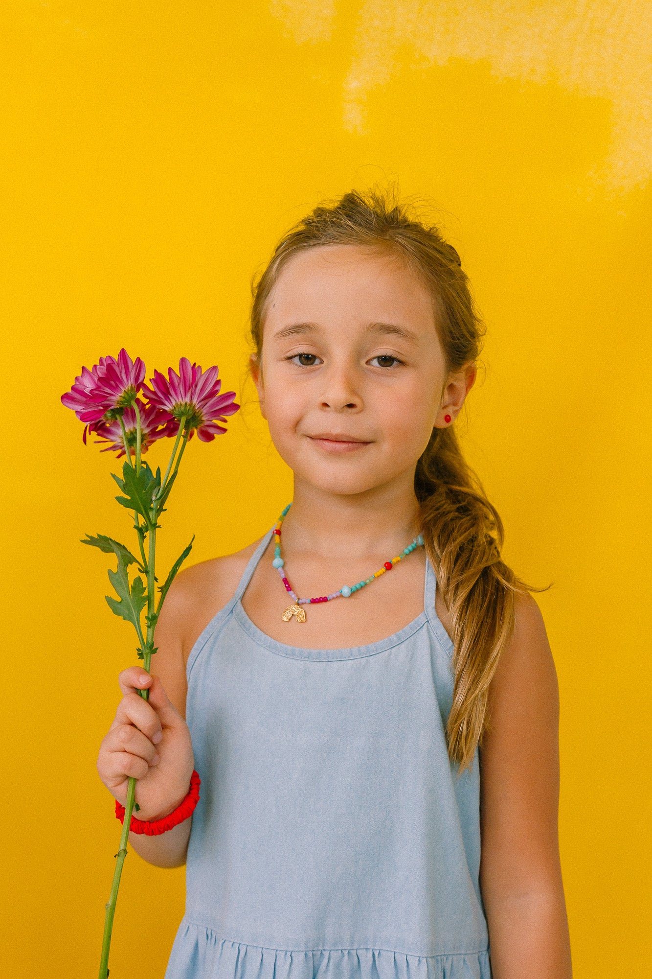 girl with rainbow necklace, holding flowers on a yellow background