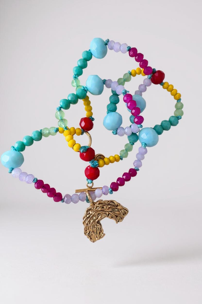 Multicolored crystal bead necklace with a gold rainbow-shaped charm on a white background.