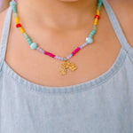 Multicolored beaded necklace with a gold rainbow-shaped pendant, worn by a girl wearing a light blue top.