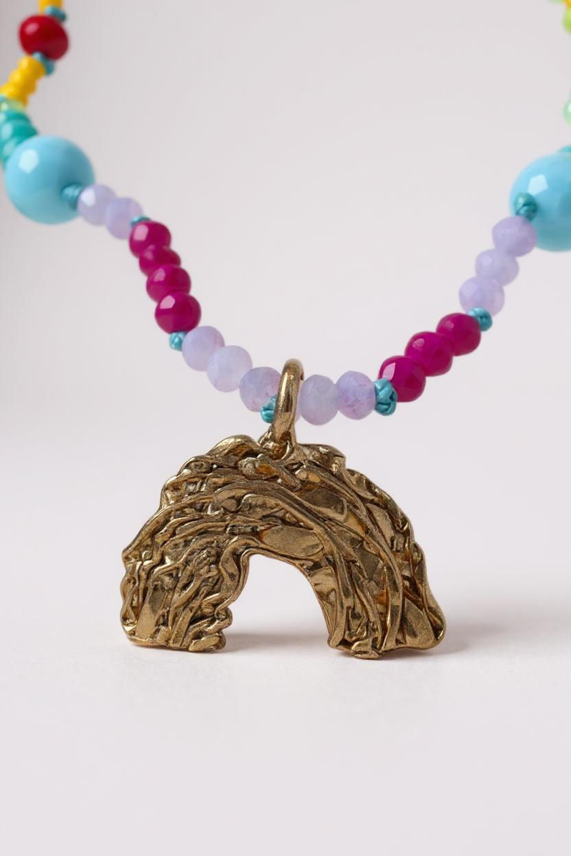 Close-up of multicolored beaded necklace with a rainbow-shaped gold pendant, on a light gray background. 