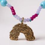 Close-up of multicolored beaded necklace with a rainbow-shaped gold pendant, on a light gray background. 