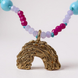 Close-up of multicolored beaded necklace with a rainbow-shaped gold pendant, on a light gray background. 