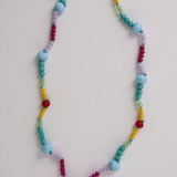 Colorful beaded necklace with a gold charm on a light gray background