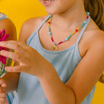 Girl in half profile wearing a colorful necklace and holding a pink flower on a yellow background.