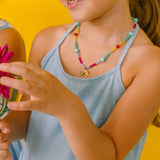 Girl in half profile wearing a colorful necklace and holding a pink flower on a yellow background.