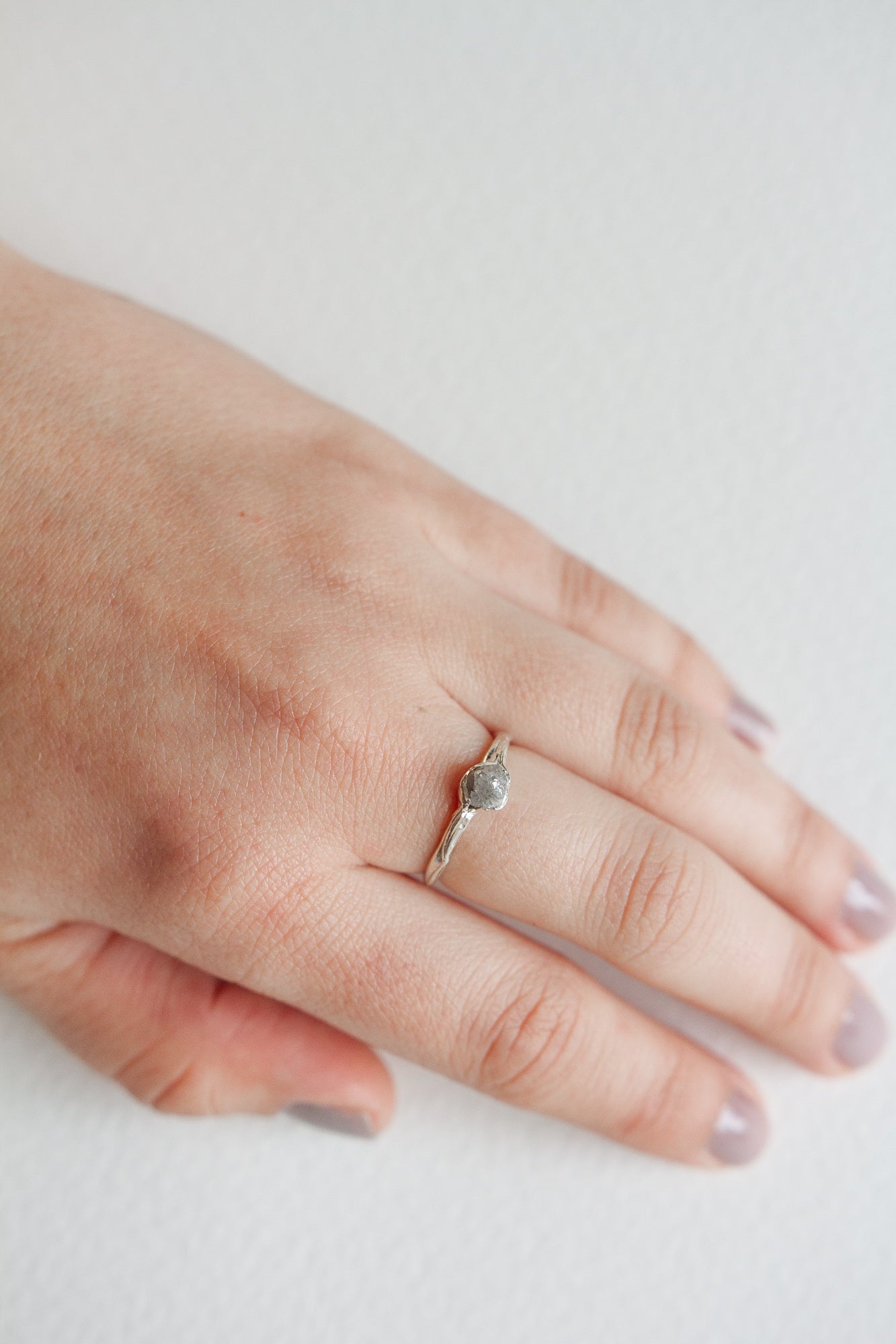 Hand wearing a silver ring with a central textured stone, showcasing its delicate and organic design.