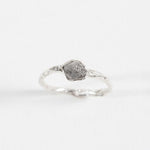 Side view of a silver ring with a rugged, natural-looking stone setting, placed on a white background.