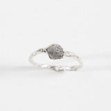 Side view of a silver ring with a rugged, natural-looking stone setting, placed on a white background.