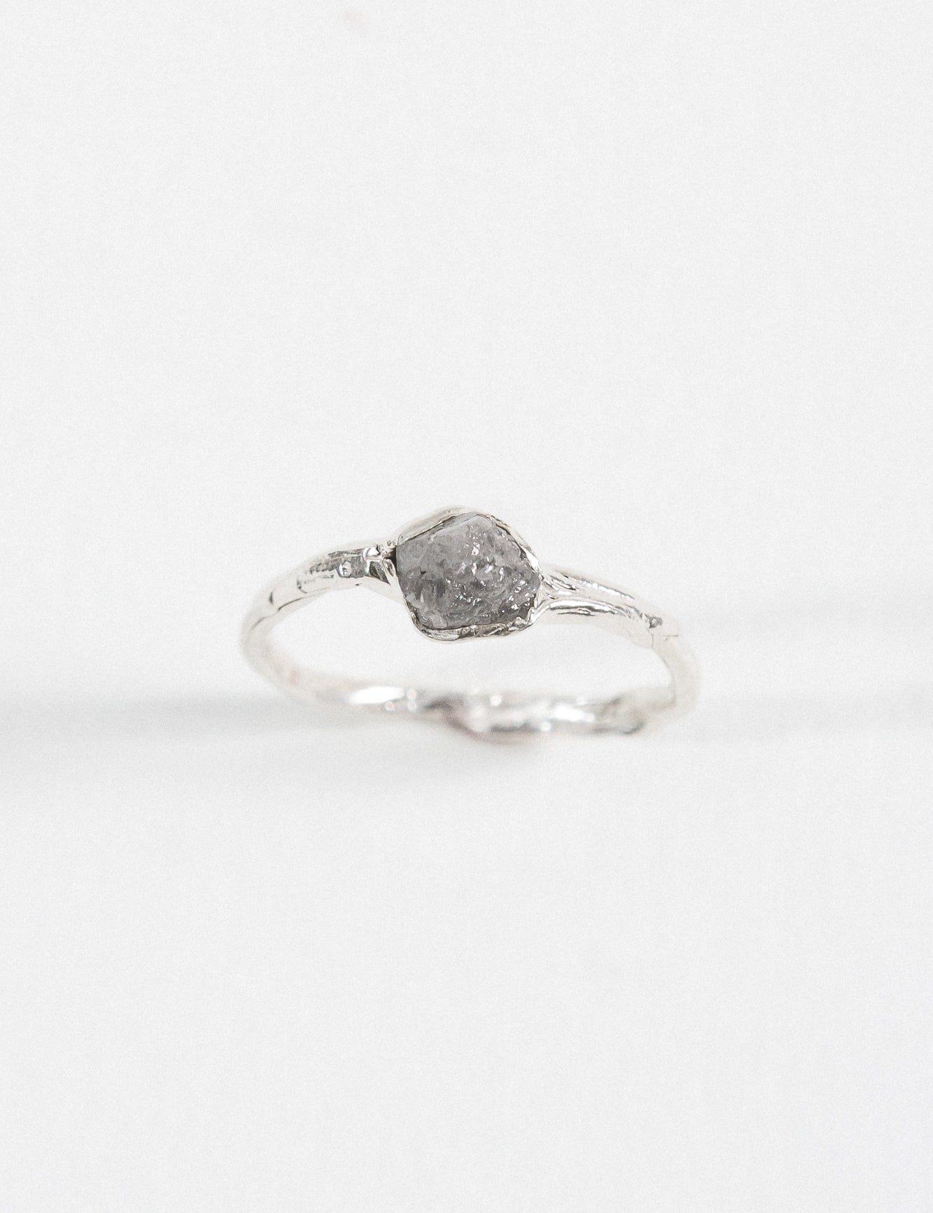 Side view of a silver ring with a rugged, natural-looking stone setting, placed on a white background.