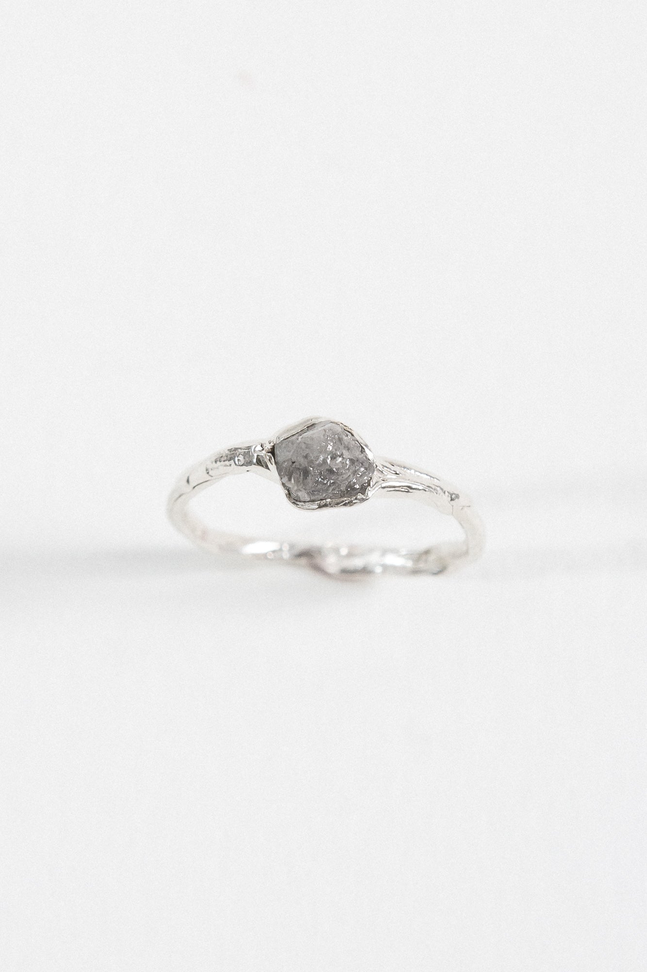 Side view of a silver ring with a rugged, natural-looking stone setting, placed on a white background.