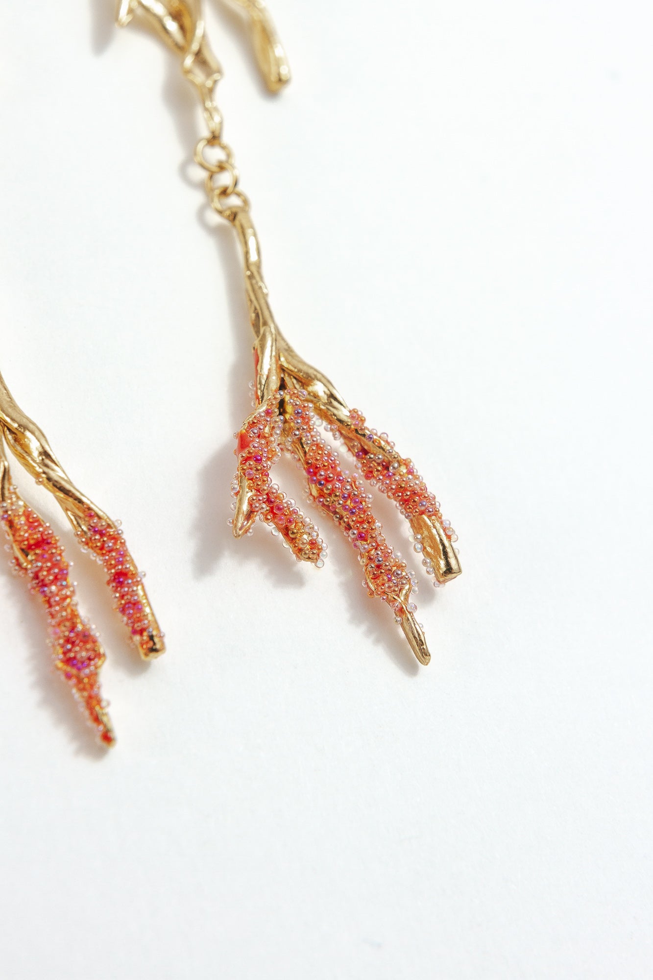 Close-up detail of the Root Earrings in red, with hand-painted coral-colored glass granulation.