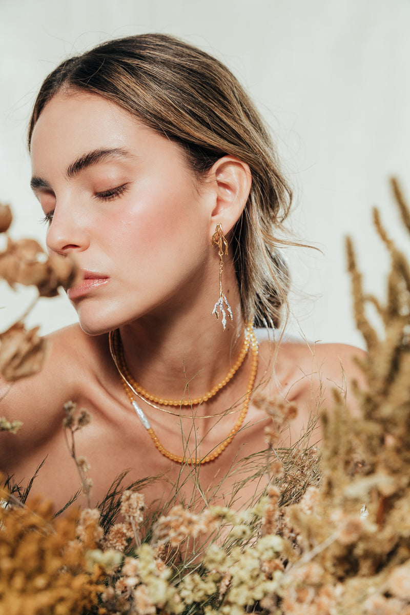 Model wearing the Root Earrings in a natural setting with foliage, highlighting the botanical and artisanal style of the jewelry.