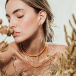 Model wearing the Root Earrings in a natural setting with foliage, highlighting the botanical and artisanal style of the jewelry.