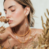 Model wearing the Root Earrings in a natural setting with foliage, highlighting the botanical and artisanal style of the jewelry.