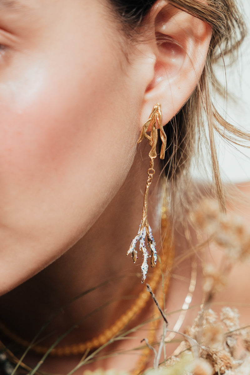 Close-up of a person wearing gold earrings with a blurred natural background