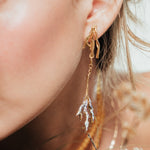 Close-up of a person wearing gold earrings with a blurred natural background