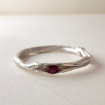 Front view of a nest ring, made of silver with a ruby in the center, on a light background.