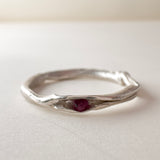 Front view of a nest ring, made of silver with a ruby in the center, on a light background.