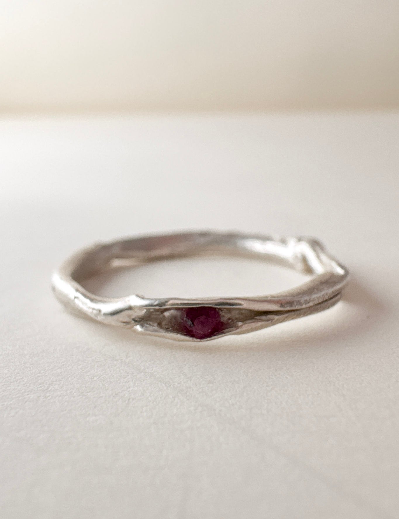 Front view of a nest ring, made of silver with a ruby in the center, on a light background.
