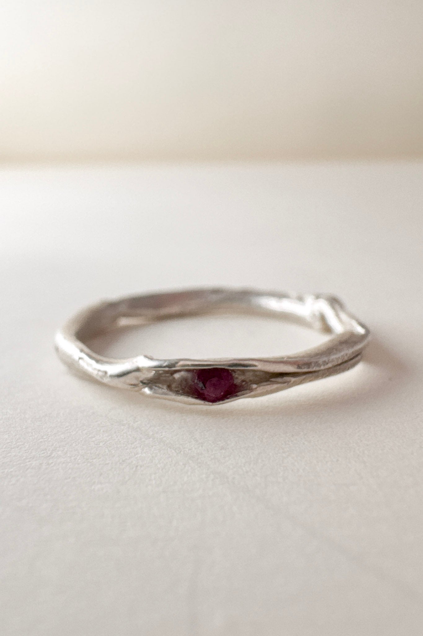 Front view of a nest ring, made of silver with a ruby in the center, on a light background.