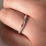 Silver ring with a red gemstone on a finger against a neutral background