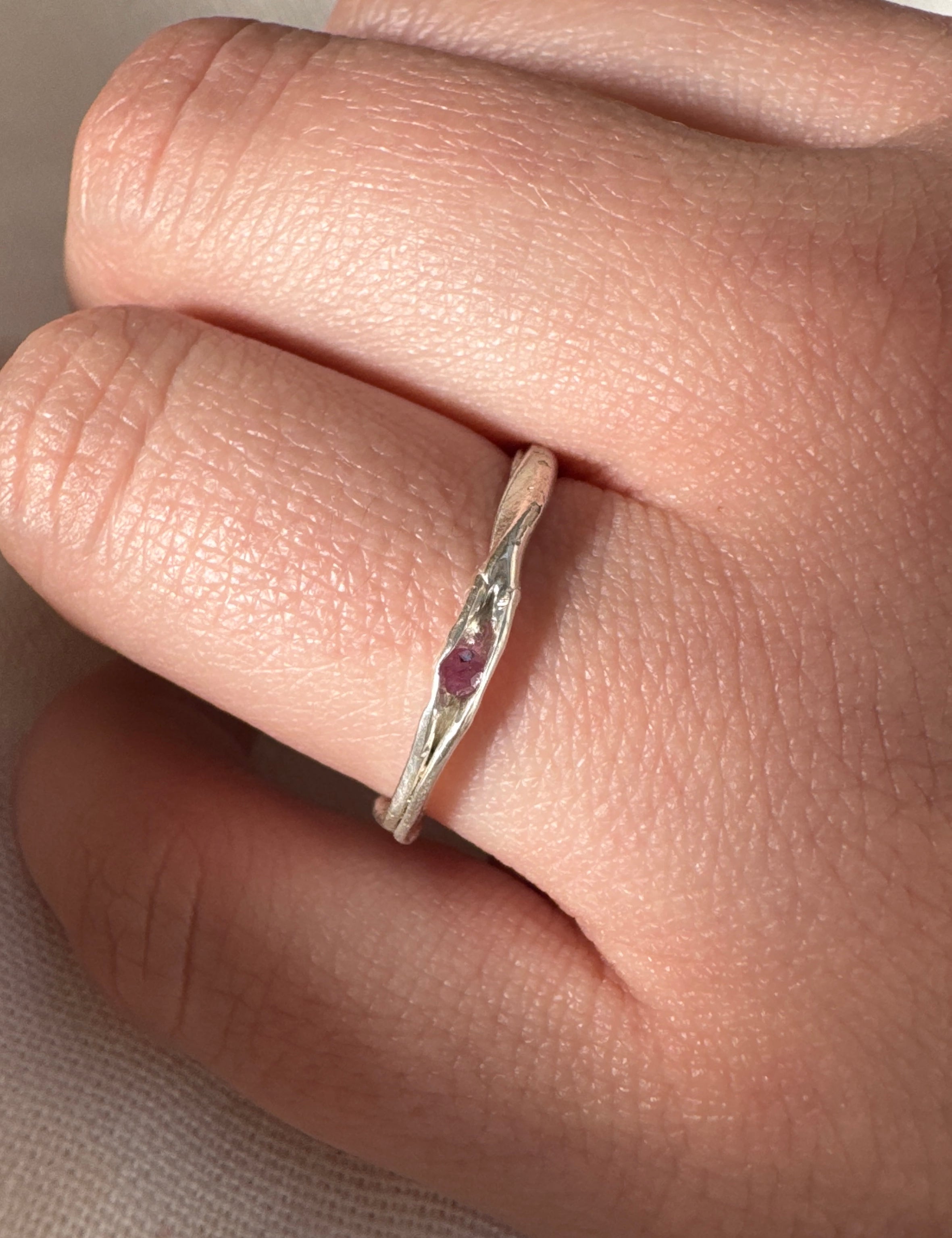 Silver ring with a red gemstone on a finger against a neutral background
