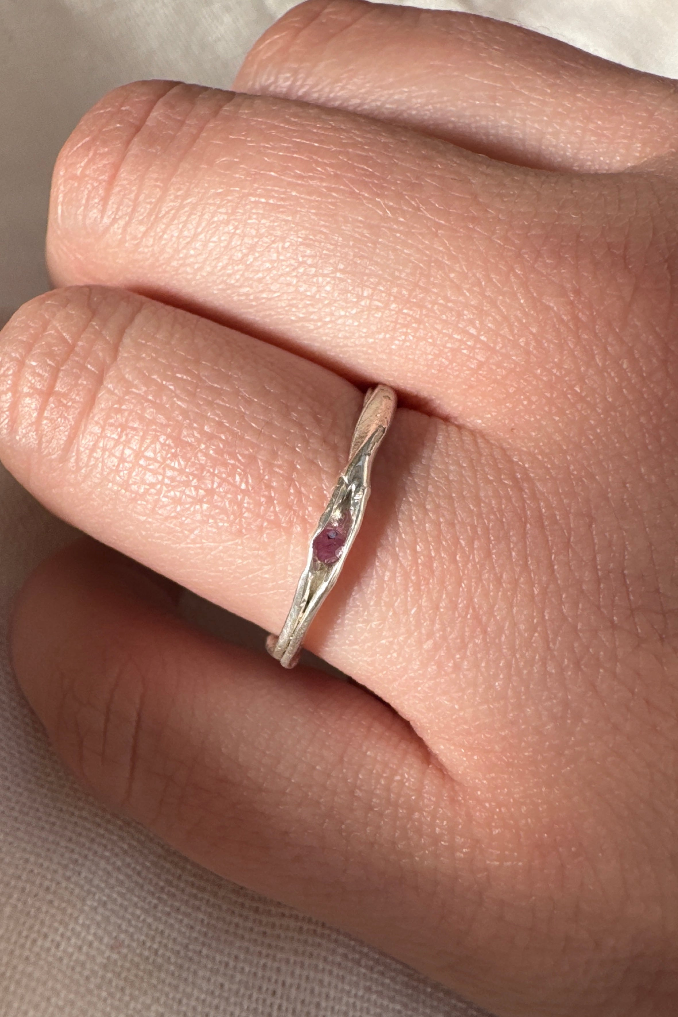 Silver ring with a red gemstone on a finger against a neutral background