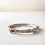 Side view of a nest ring, made of silver with a ruby in the center, on a light background.