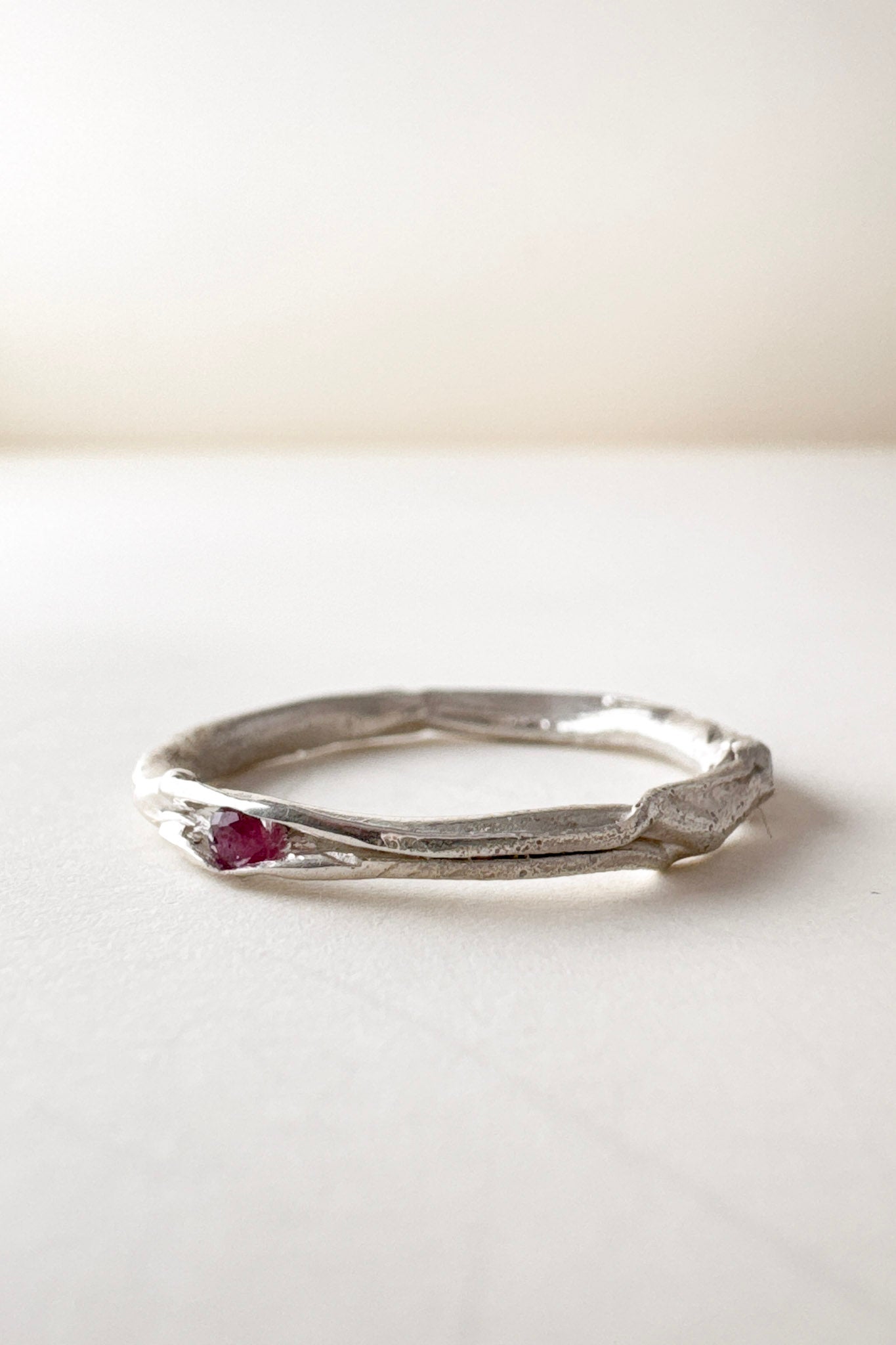 Side view of a nest ring, made of silver with a ruby in the center, on a light background.