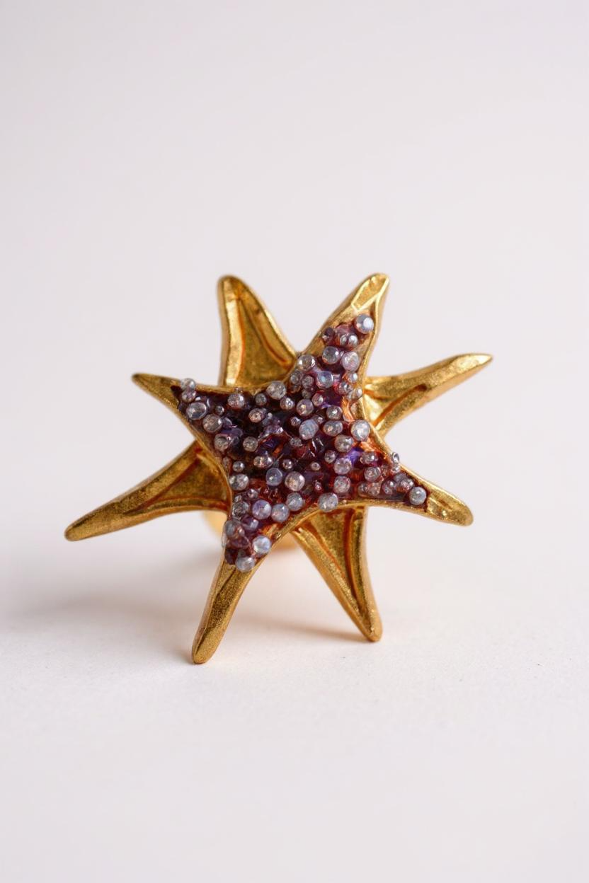 Single gold star-shaped stud earring with purple crystals on a plain white background.