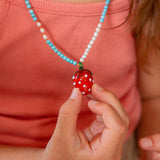 Person wearing a necklace with a strawberry pendant, holding it in their hand.