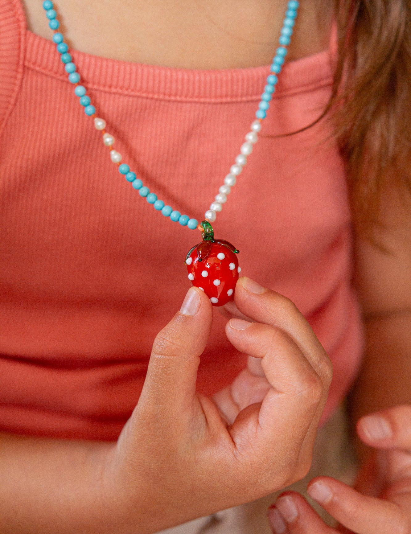 Person wearing a necklace with a strawberry pendant, holding it in their hand.