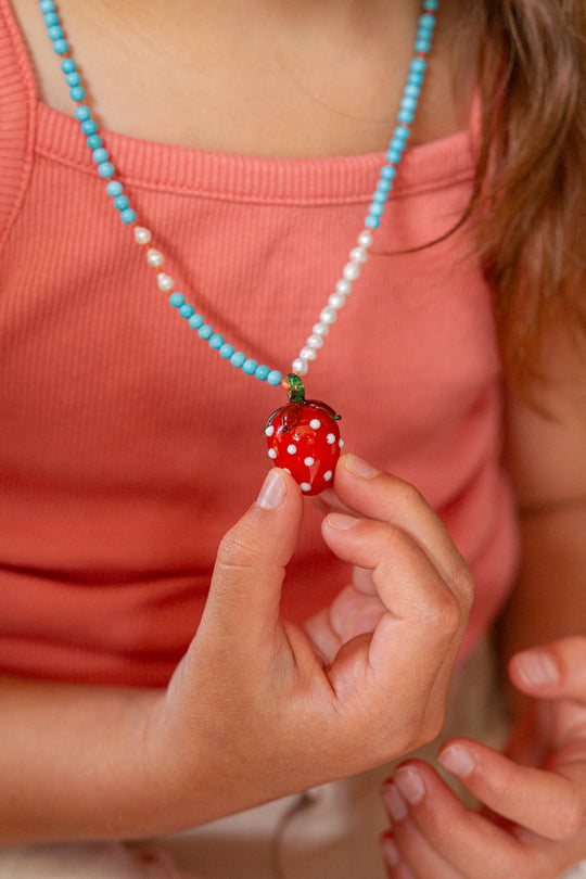 Person wearing a necklace with a strawberry pendant, holding it in their hand.