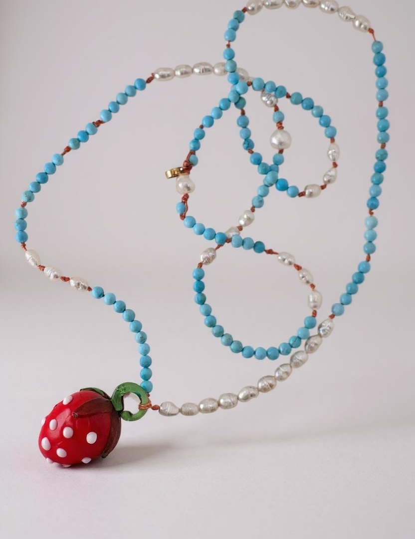 Flat lay of the Strawberry Necklace on white, showing the beaded strand coiled neatly with the red glass strawberry pendant.