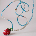 Flat lay of the Strawberry Necklace on white, showing the beaded strand coiled neatly with the red glass strawberry pendant.