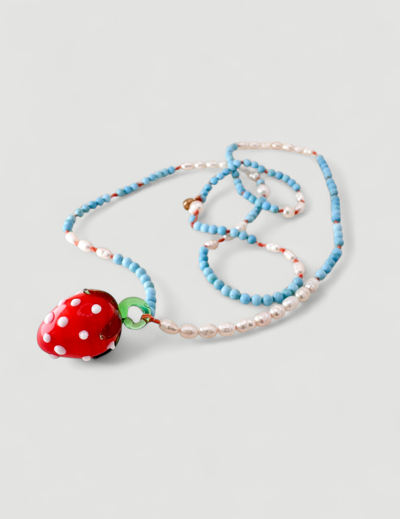 Close-up of the Strawberry Necklace charm: a blown glass strawberry with white dots, handcrafted to give a magical touch to the jewelry.