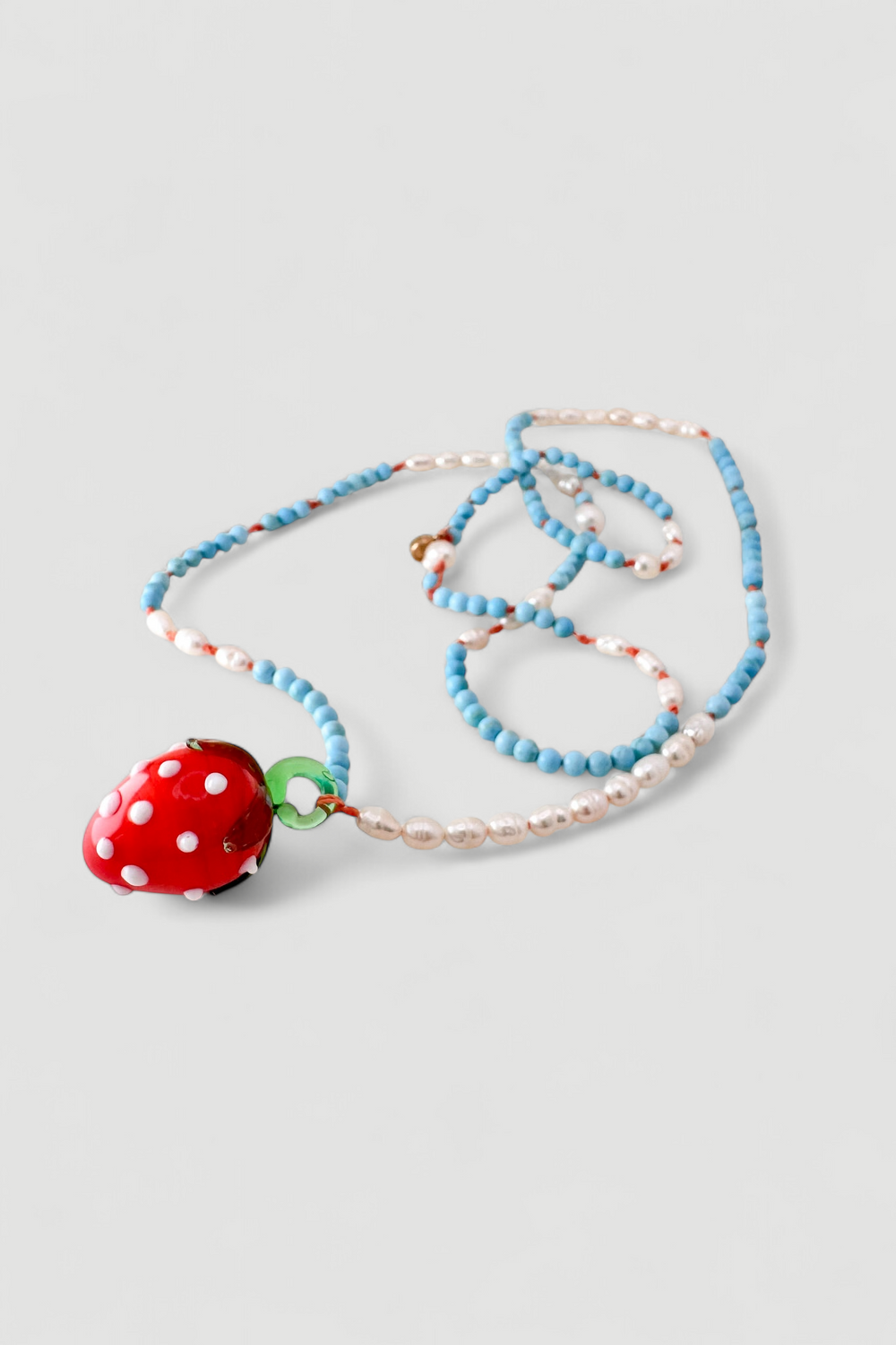 Close-up of the Strawberry Necklace charm: a blown glass strawberry with white dots, handcrafted to give a magical touch to the jewelry.