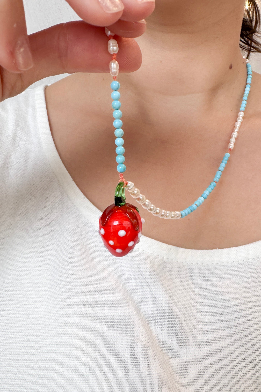 Close‑up torso shot of a child wearing a white sleeveless top and the Strawberry Necklace, with the red strawberry pendant centered.