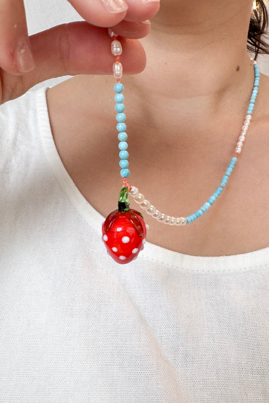 Close‑up torso shot of a child wearing a white sleeveless top and the Strawberry Necklace, with the red strawberry pendant centered.