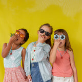 Three young girls standing together against a yellow wall, each wearing the Strawberry Necklace with the pendant hanging at varying heights.