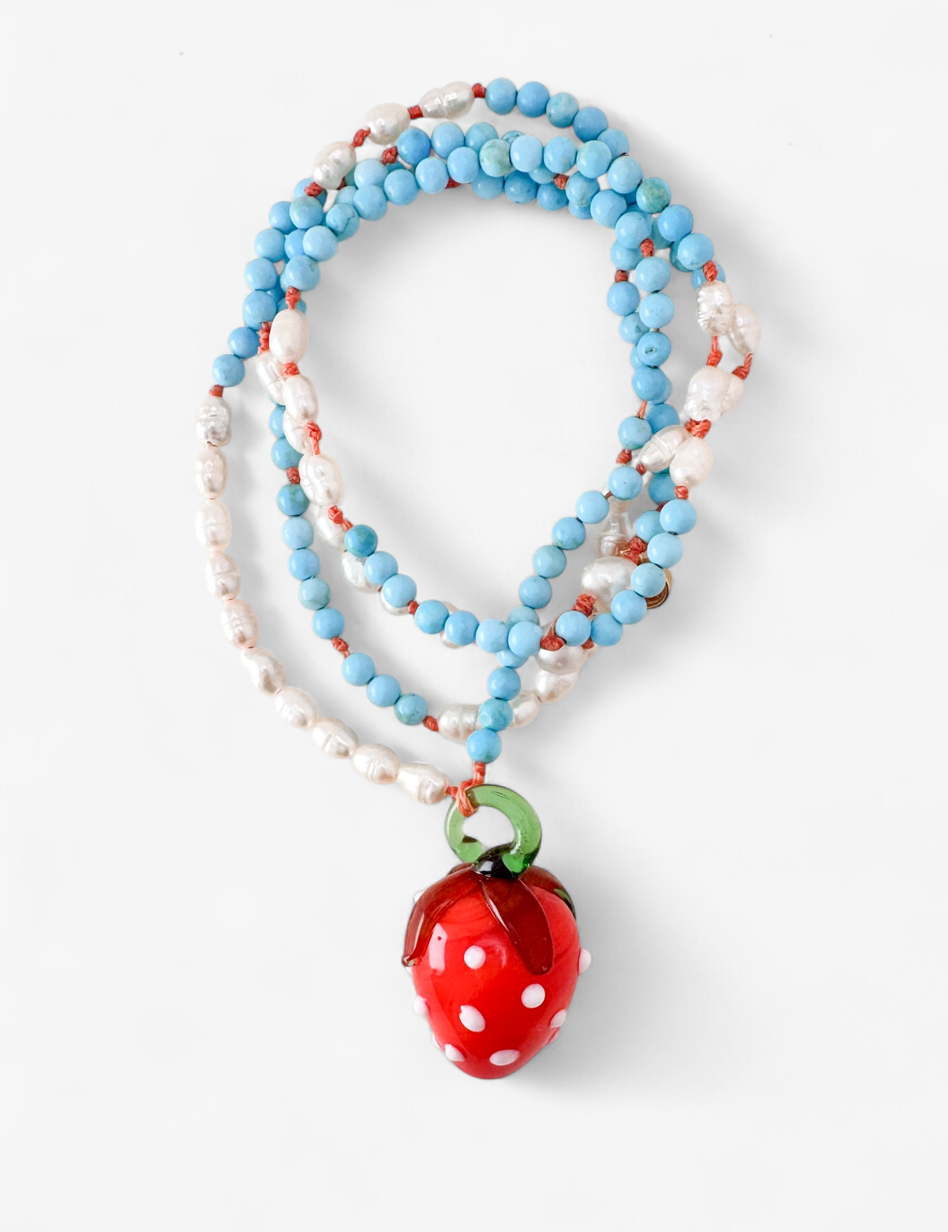 Coiled Strawberry Necklace on a white background, showcasing multiple loops of turquoise and white beads with the red glass strawberry pendant in view