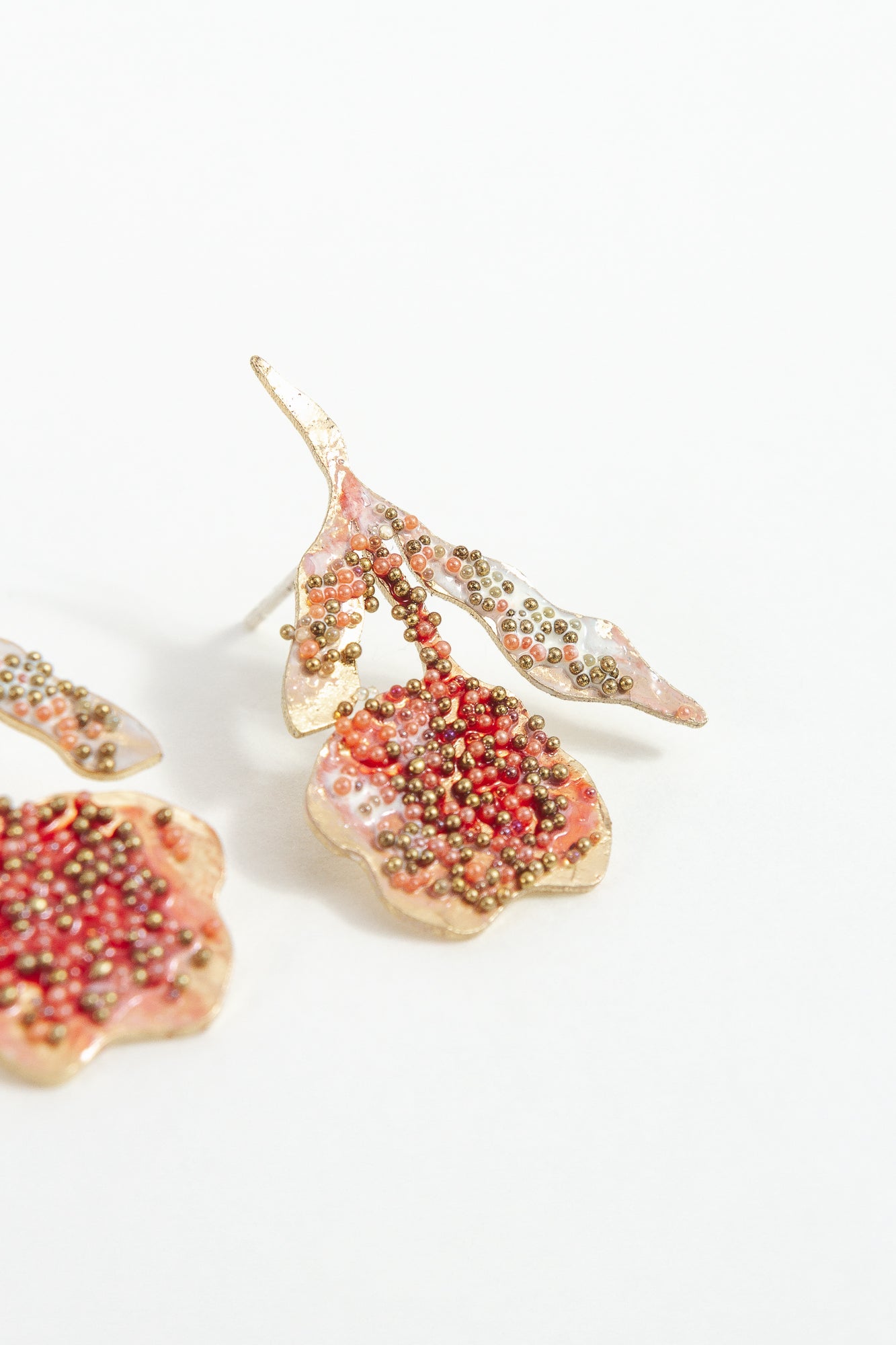 Macro detail of the red elderberry stud earrings highlighting glass granulation, artisanal texture, and coral paint.