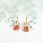 Red elderberry moths in gold-plated brass with coral petals, photographed on a white background with soft botanical shadows.