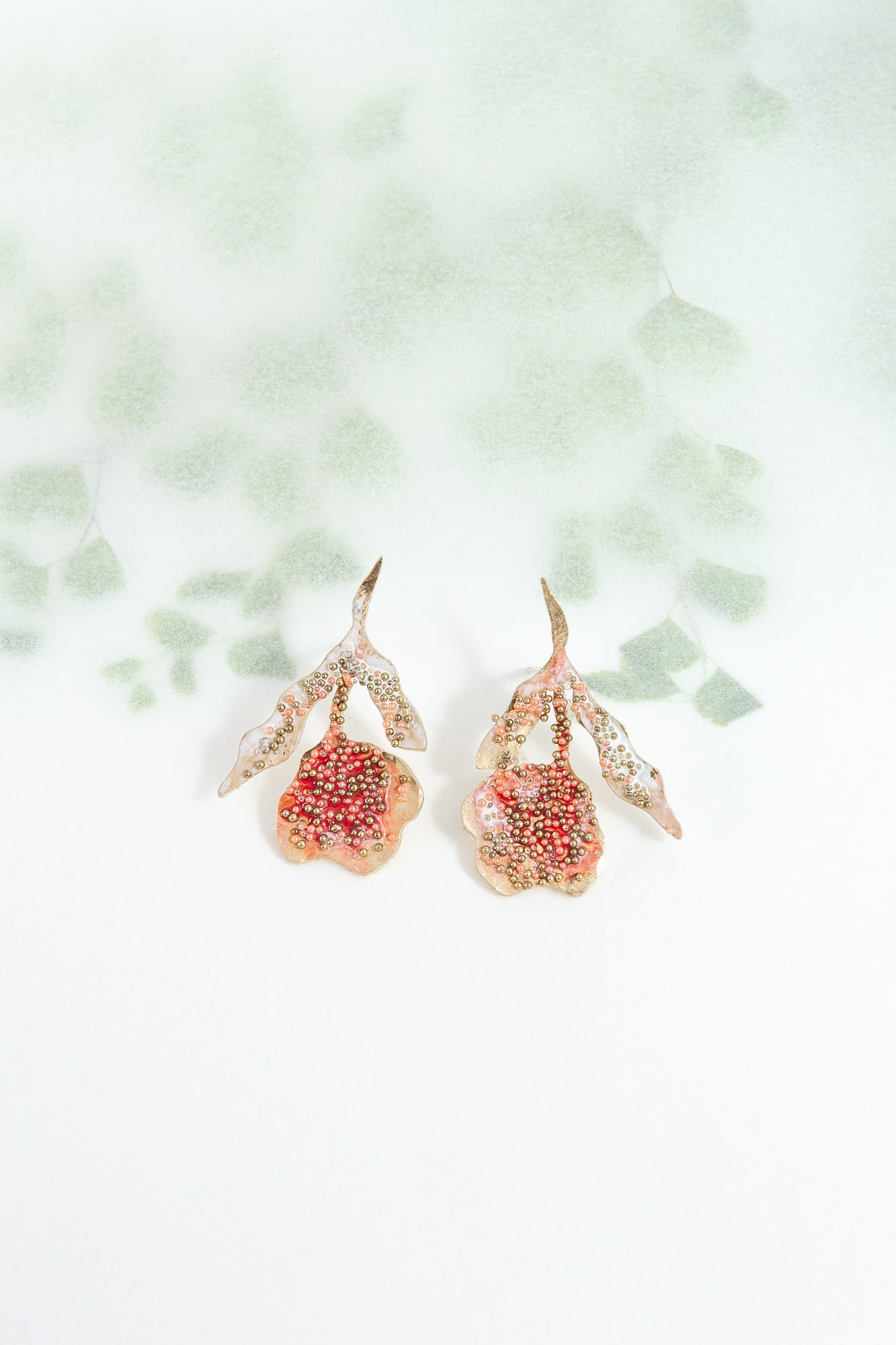 Red elderberry moths in gold-plated brass with coral petals, photographed on a white background with soft botanical shadows.