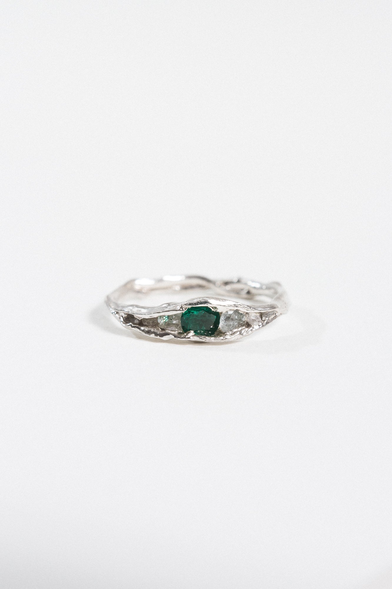 Top view of a silver ring with a textured band and an oval green gemstone.