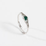 Silver ring with an organic band and a deep green gemstone, photographed on a white background