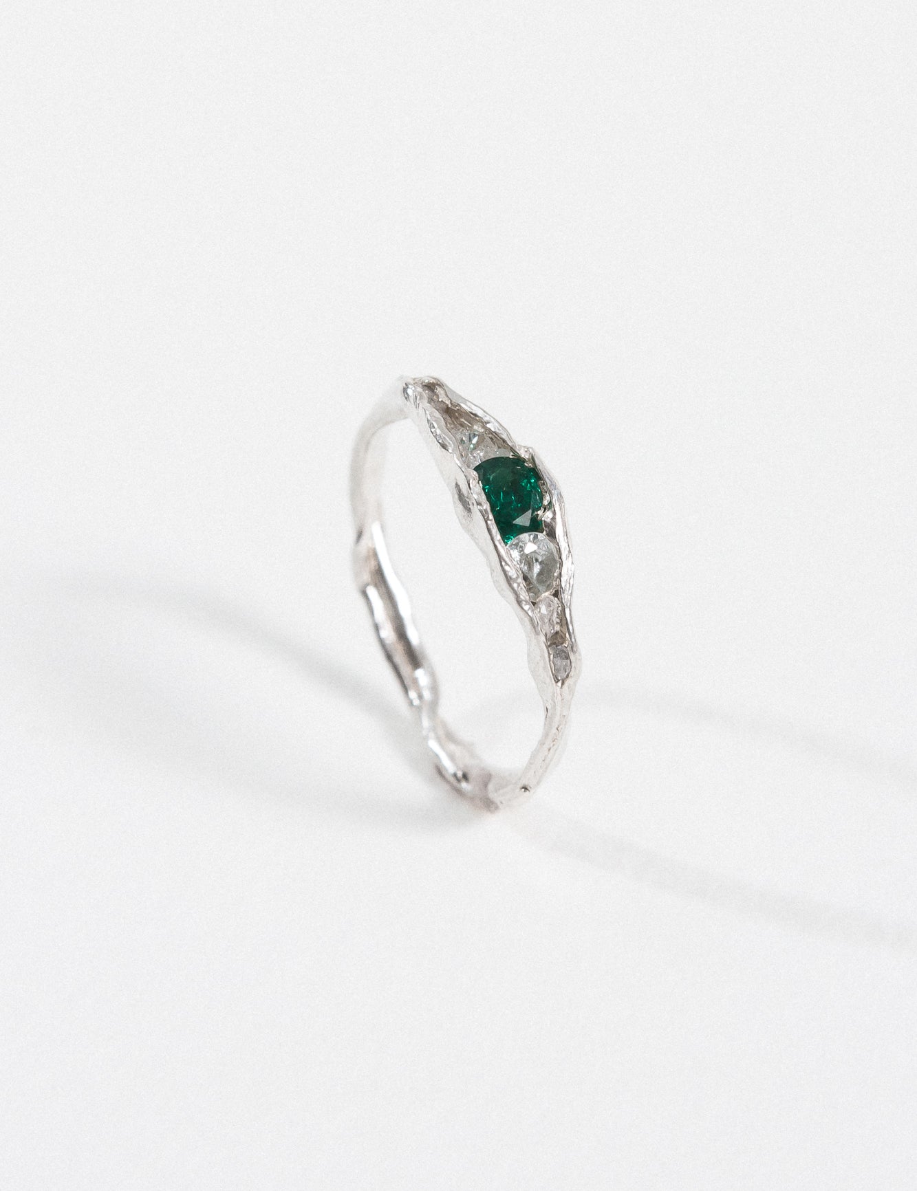 Silver ring with an organic band and a deep green gemstone, photographed on a white background