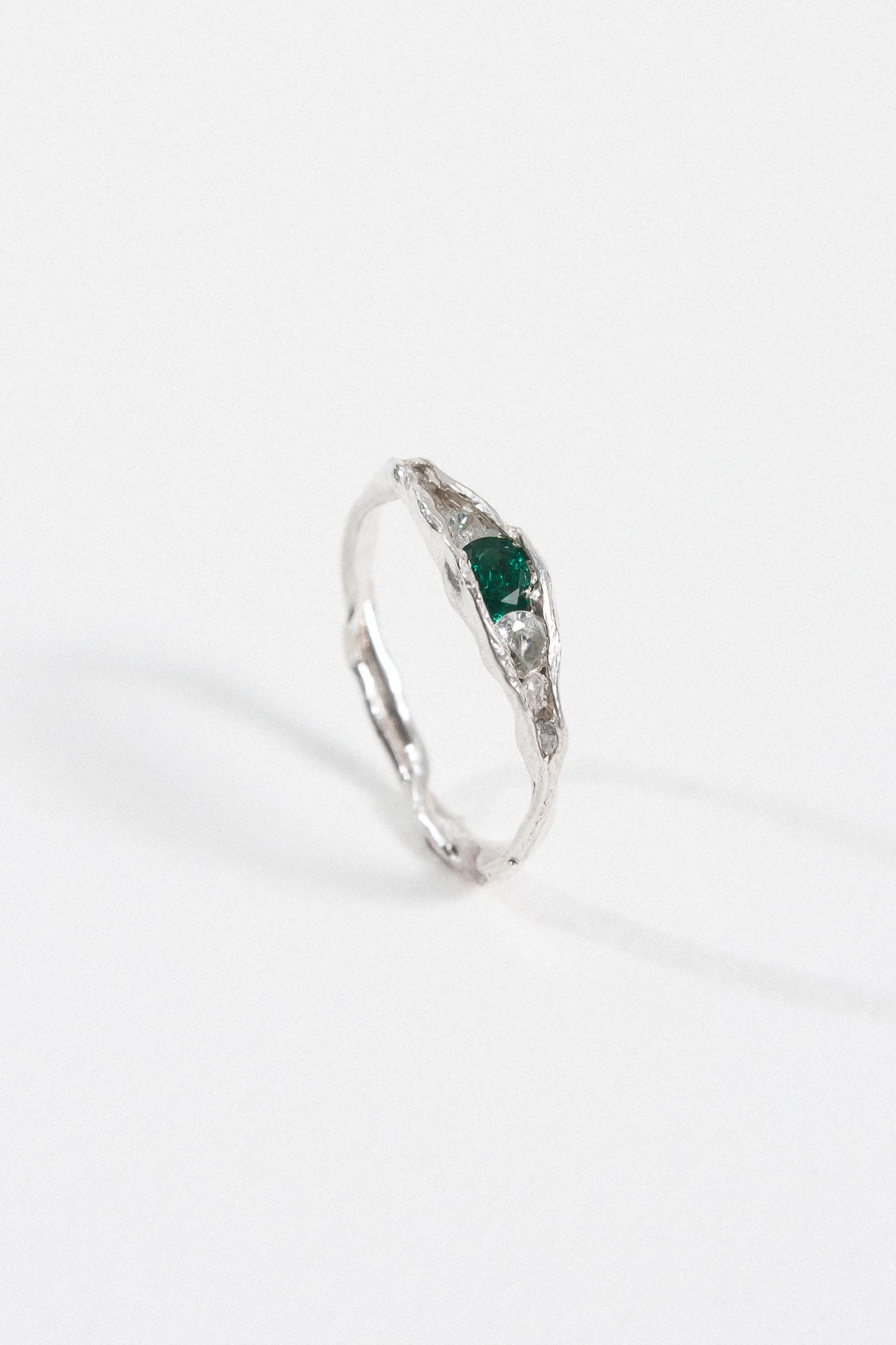 Silver ring with an organic band and a deep green gemstone, photographed on a white background