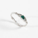 Angled view of a handcrafted silver ring with a green gemstone, placed on a white surface.