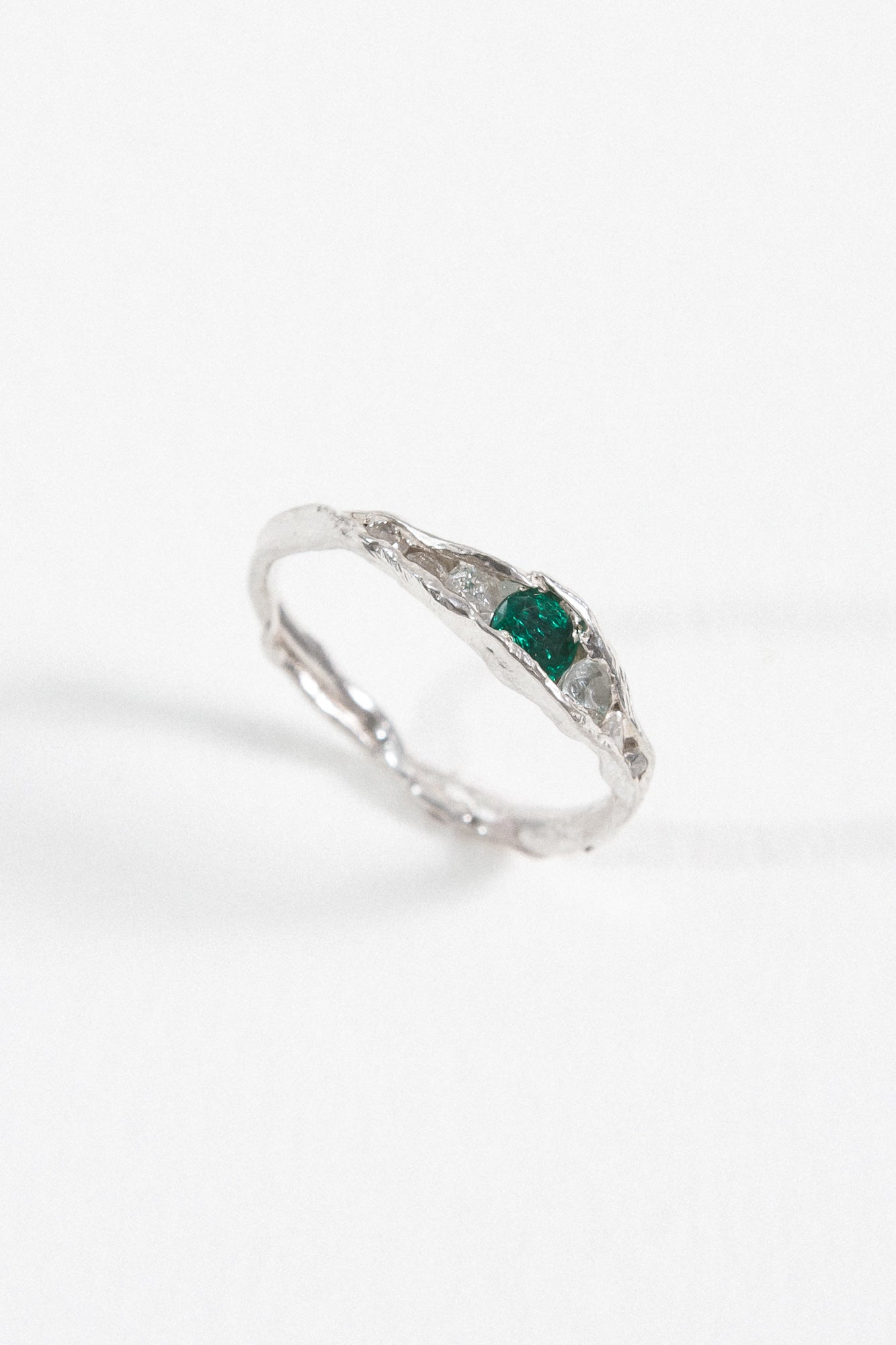 Angled view of a handcrafted silver ring with a green gemstone, placed on a white surface.